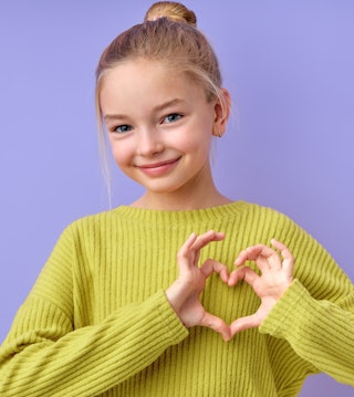Young girl making heart gesture with fingers on purple backdrop