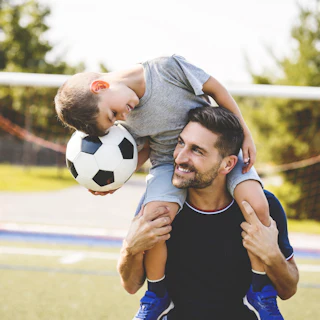 A man with child playing football outside on field