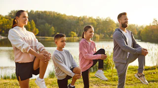 Fit and active happy parents with two kids boy and girl doing sport exercises in nature. Smiling family in sportswear having workout in the park. Outdoors training and fitness concept.
