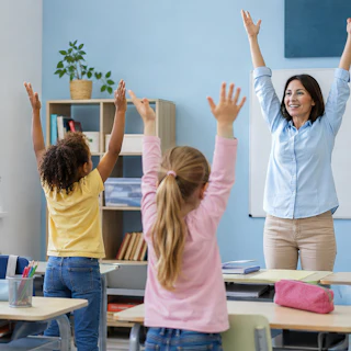 Teacher leading children in a classroom movement break. Group of students doing physical exercise with arms raised. Education, health and active learning concept in elementary school.