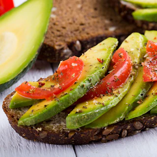 Avocado sandwich with tomato and seasoning on dark rye bread.