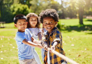 Fun, games and kids playing tug of war together outdoor in a park or playground in summer. Friends, diversity and children pulling a rope while being playful fun or bonding in a garden on a sunny day.